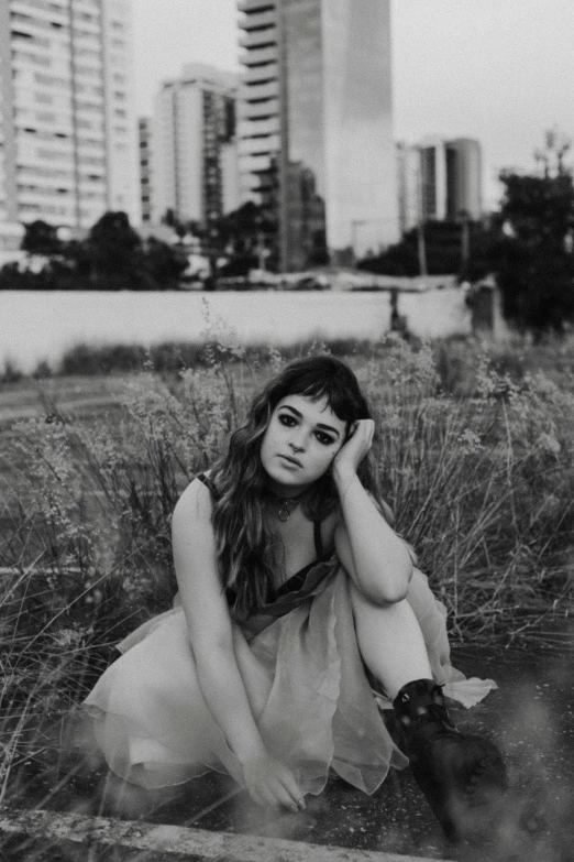 a black and white photo of a woman in a field, by Amelia Peláez, joey king, in sao paulo, sitting pose, in the city