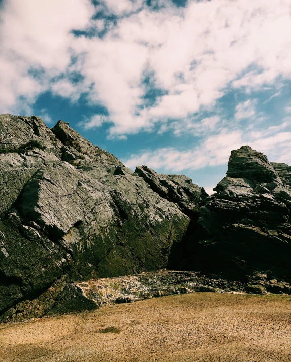 a man riding a skateboard on top of a sandy beach, an album cover, unsplash, large rocks with thick moss, ((rocks)), pembrokeshire, mountainous