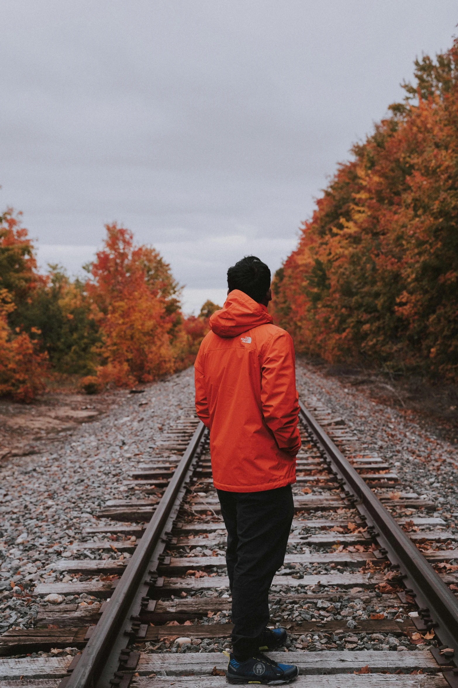 a man in an orange jacket standing on a train track, unsplash contest winner, fall foliage, facing away from camera, profile image, profile picture