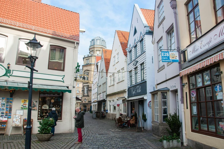 a woman is walking down a cobblestone street, by Breyten Breytenbach, pexels contest winner, art nouveau, white buildings with red roofs, detmold, coastal, beige