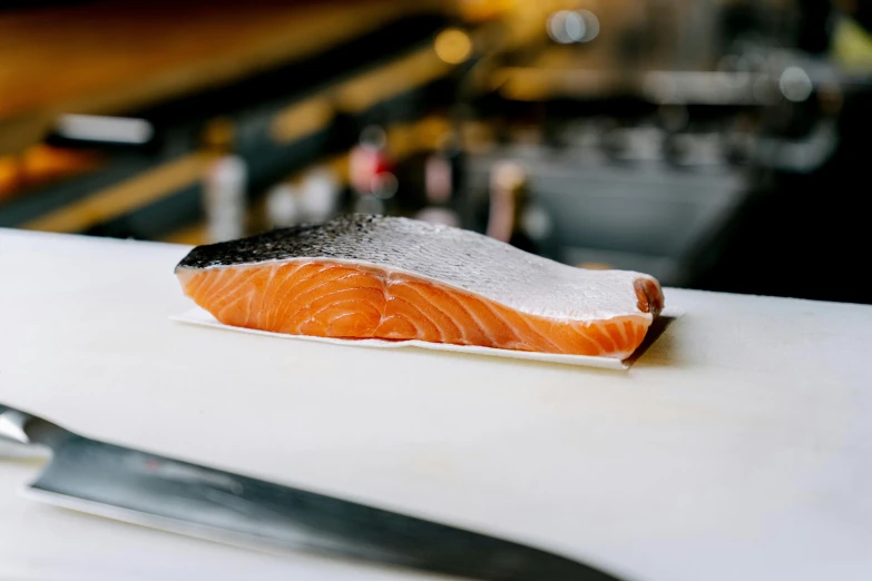 a piece of salmon sitting on top of a cutting board, a picture, by Tom Bonson, trending on pexels, sōsaku hanga, at the counter, facing sideways, from street level, 🦩🪐🐞👩🏻🦳