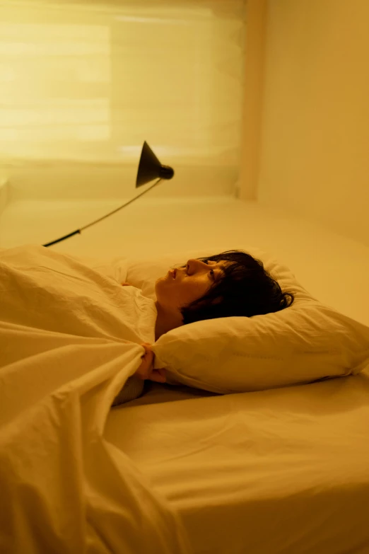 a woman laying on top of a bed under a blanket, inspired by Nan Goldin, unsplash, conceptual art, yellow lighting from right, humans sleeping in healing pods, sangsoo jeong, emerging from her lamp