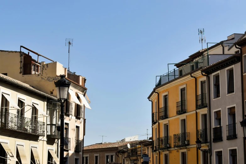 a group of people walking down a street next to tall buildings, inspired by Josep Rovira Soler, unsplash, view of villages, clear blue sky, square, preserved historical