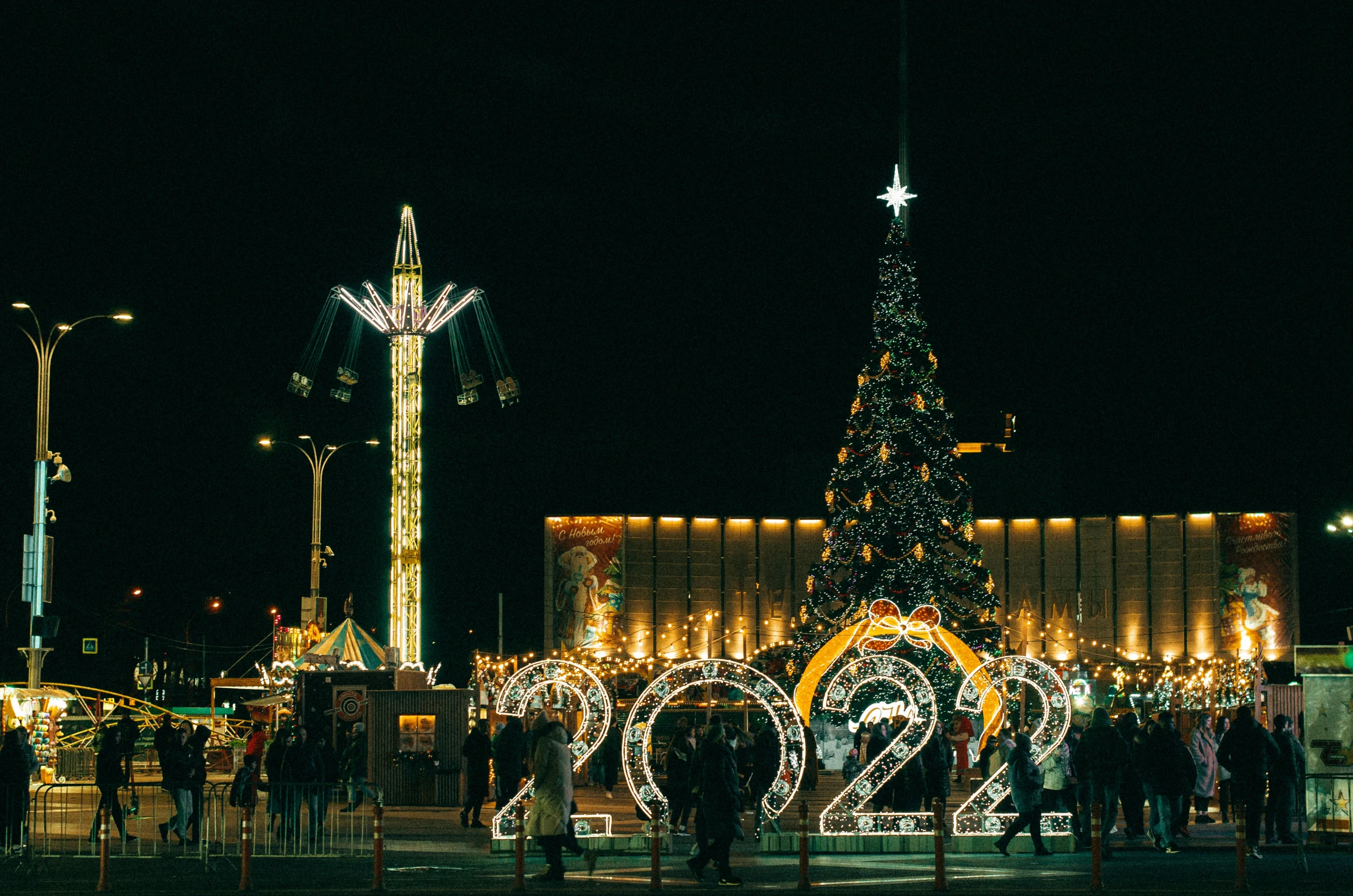 a group of people standing in front of a christmas tree, by Julia Pishtar, pexels contest winner, happening, rostov city, few neon signs, photo of the year 2 0 2 2, park in background