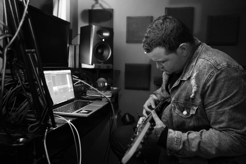 a man playing a guitar in front of a laptop, by Matt Cavotta, studio recording, structure : kyle lambert, b&w photo, uploaded