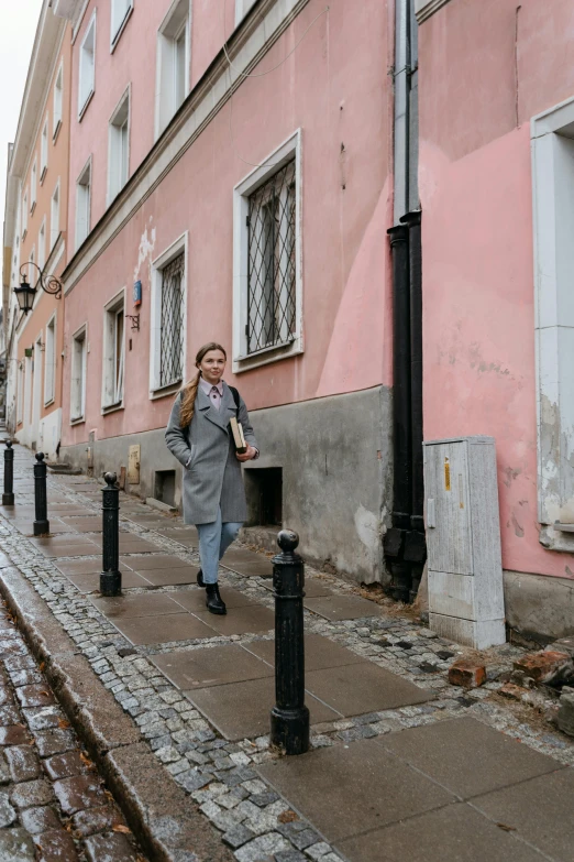 a woman walking down a street talking on a cell phone, by Emma Andijewska, pexels contest winner, socialist realism, pink marble building, capital of estonia, wearing trenchcoat, in front of the house