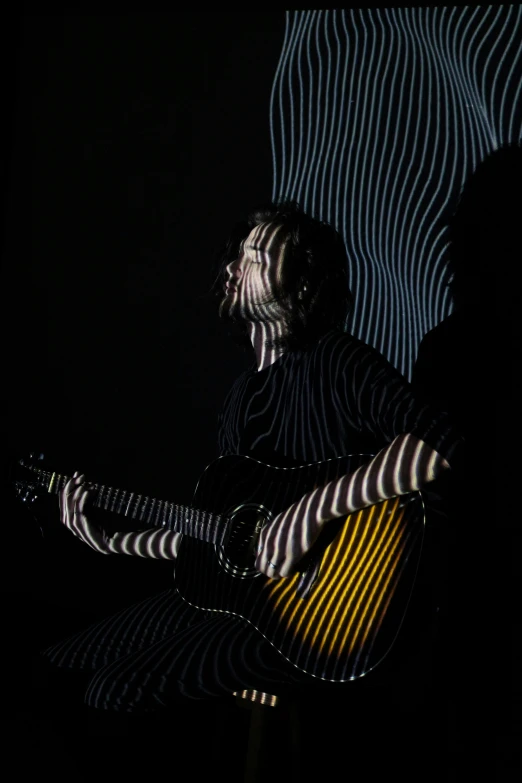 a man sitting in a chair playing a guitar, an album cover, unsplash, conceptual art, refracted lighting, white stripes all over its body, standing with a black background, glow wave