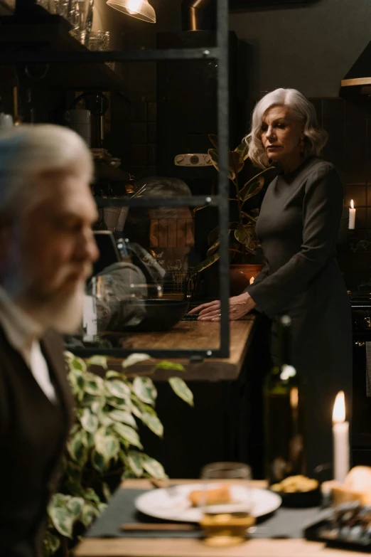 a woman standing in a kitchen next to a man, a still life, trending on pexels, magical realism, silver hair and beard, dark sci - fi movie scene, [ theatrical ]