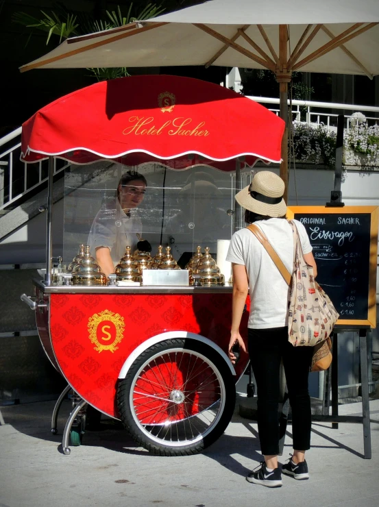 a woman standing in front of a food cart, gold and red accents, stroopwaffel, sunny day time, thumbnail