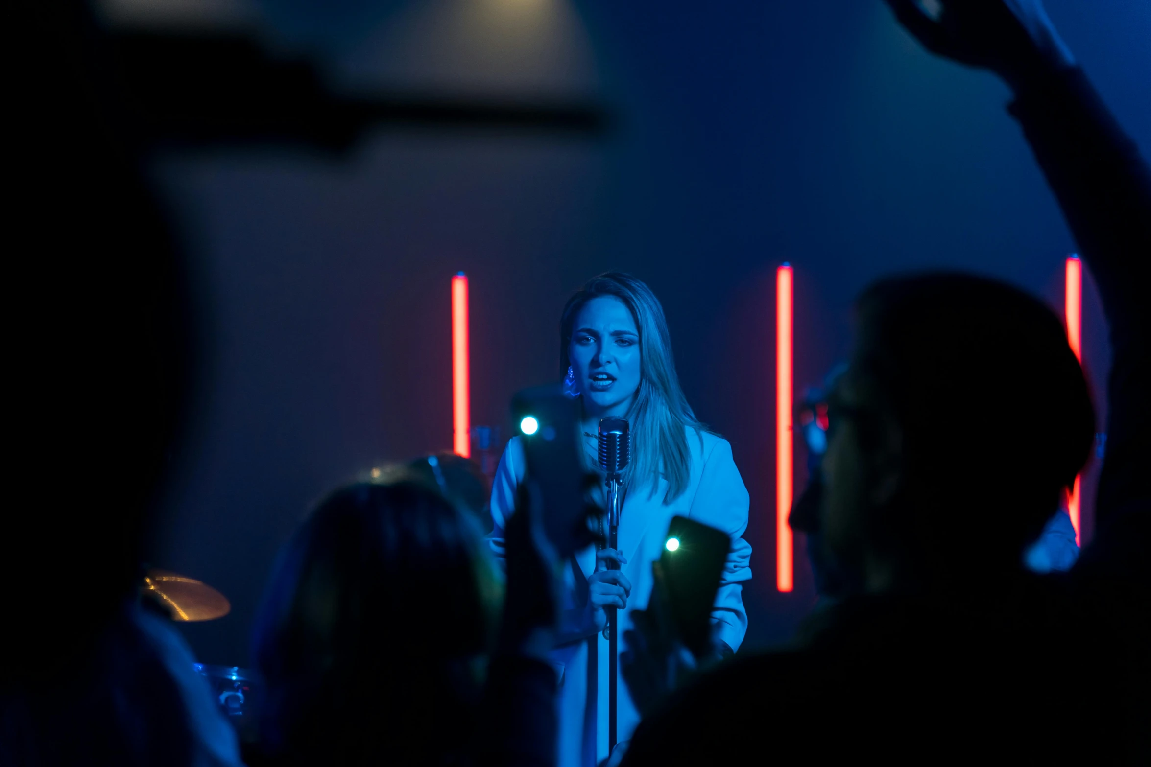 a woman that is standing in front of a microphone, performing a music video, a group of people, cinematic mood lighting, taken with sony alpha 9