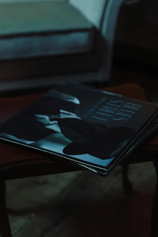 a magazine sitting on top of a wooden table, an album cover, inspired by Elsa Bleda, unsplash, extremely moody blue lighting, sullen, in a dark dusty parlor, low angle shot
