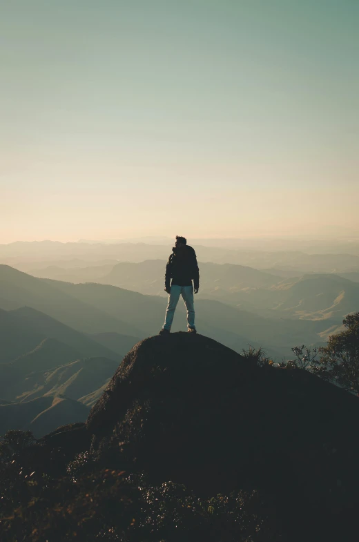 a person standing on top of a mountain, facing away from the camera, gazing off into the horizon, candid photography, distant full body view