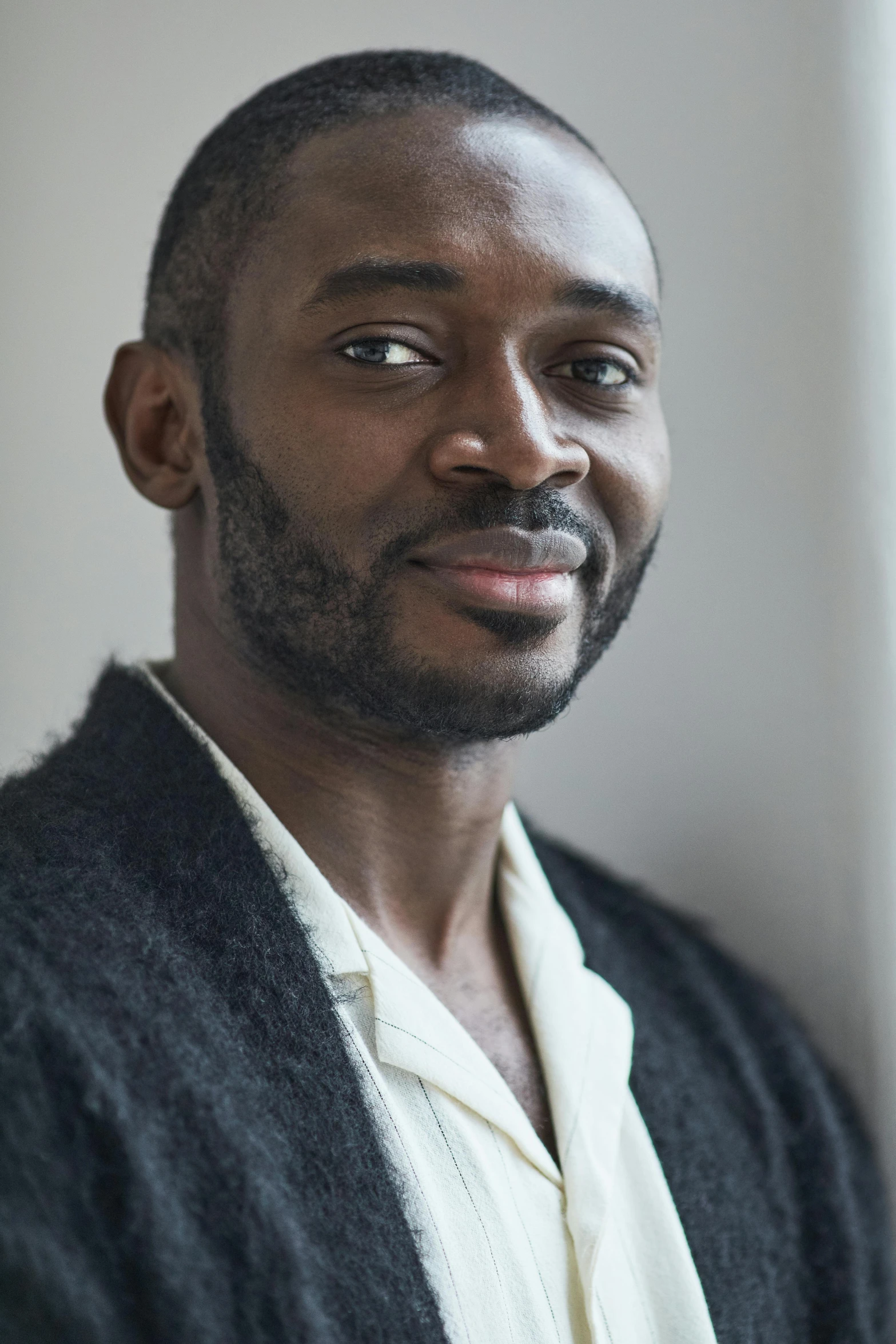 a man standing in front of a window, an album cover, inspired by Theo Constanté, closeup headshot portrait, wearing a grey robe, adebanji alade, herzog de meuron