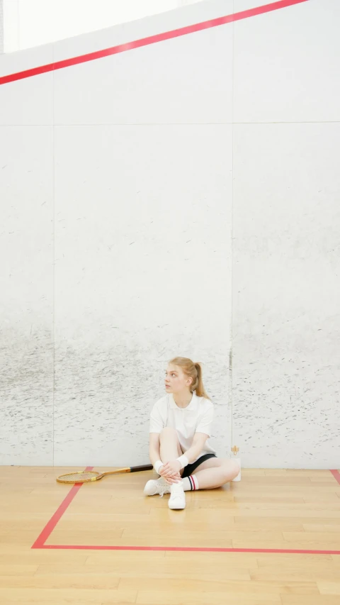 a woman sitting on top of a wooden floor holding a racquet, a picture, inspired by Louisa Matthíasdóttir, unsplash, minimalism, petra cortright, ballet, ellie bamber, low quality photo