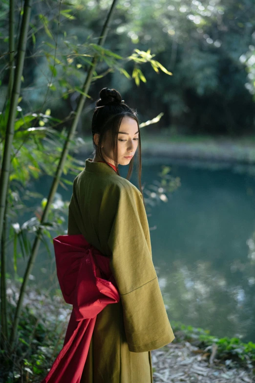 a woman in a kimono standing next to a body of water, inspired by Gu An, unsplash contest winner, green robes, wearing a scarlet hoodie, li bingbing, katanas strapped to her back