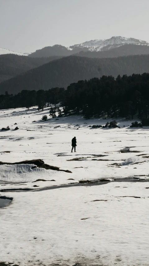 a person walking across a snow covered field, a black and white photo, pexels contest winner, land art, overlooking a desolate wasteland, instagram photo, in an icy river, in mountains