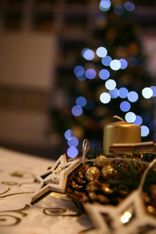 a candle sitting on top of a table next to a christmas tree, blue and yellow glowing lights, gold dappled light, in detail, on a table