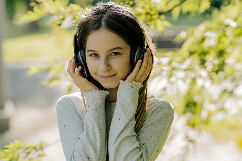 a beautiful young woman talking on a cell phone, an album cover, by Emma Andijewska, trending on pexels, hurufiyya, dafne keen, girl wearing headphones, in the park, lovingly looking at camera