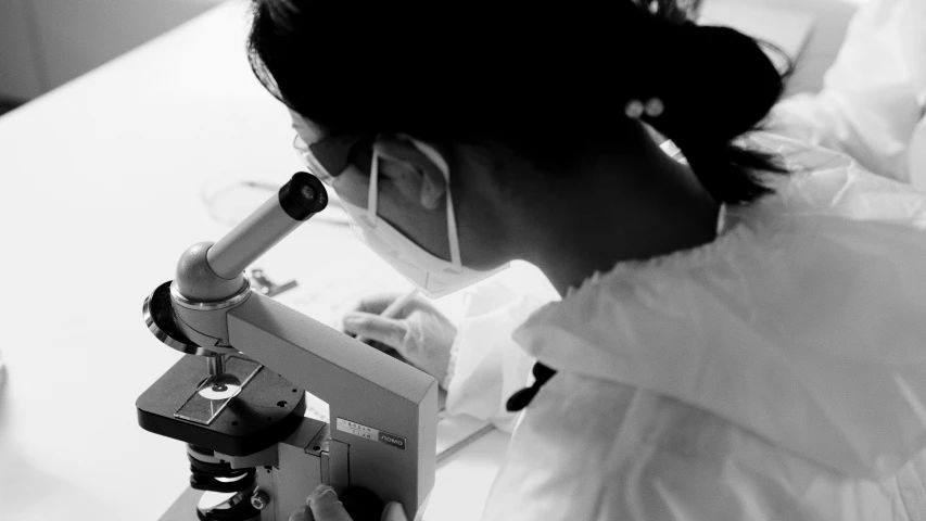 a black and white photo of a woman looking through a microscope, a microscopic photo, by Adam Marczyński, pexels, wearing lab coat, hd footage, ::