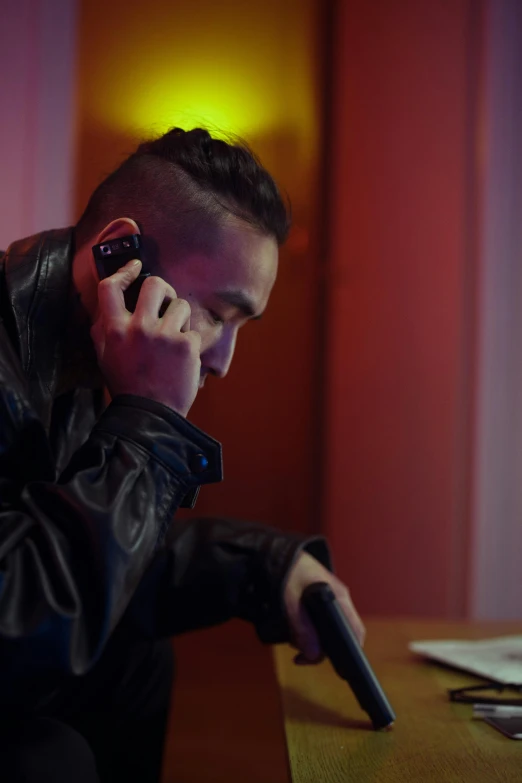 a man sitting at a table talking on a cell phone, inspired by Li Tiefu, happening, in a nightclub, wearing samcrow leather jacket, worksafe. cinematic, lgbtq