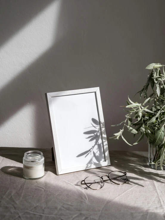 a picture frame sitting on top of a table next to a plant, inspired by Robert Mapplethorpe, unsplash contest winner, light and space, silver silver glasses, white tablecloth, photoshoot for skincare brand, mid morning lighting