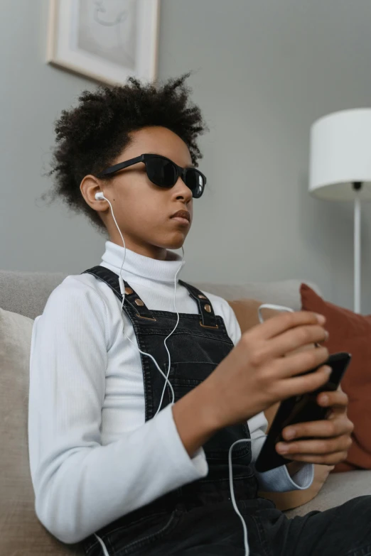 a person sitting on a couch with headphones on, trending on pexels, afrofuturism, portrait of 14 years old boy, digital sunglasses, genderless, sophisticated