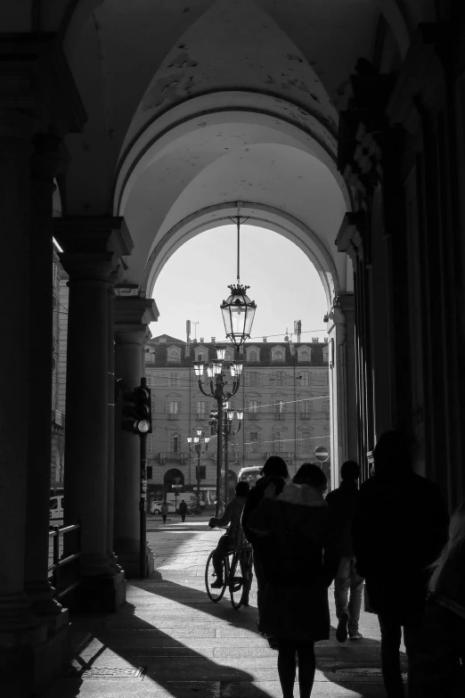 a black and white photo of people walking through an archway, a black and white photo, neoclassicism, sitting in a cafe, street lamps, palace of the chalice, late afternoon lighting