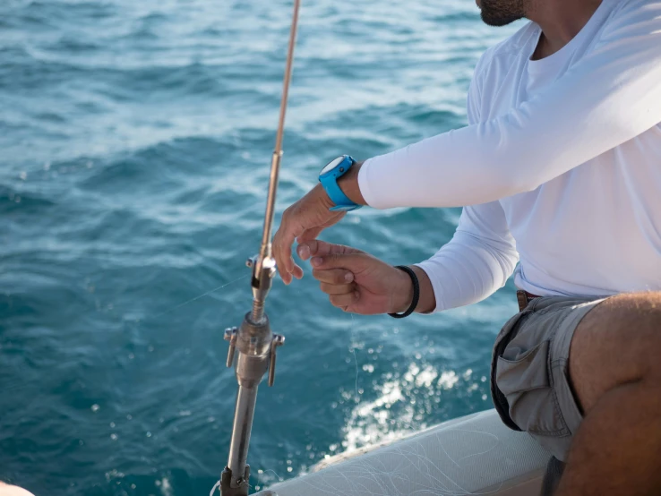 a man that is sitting on a boat in the water, spiked wristbands, filleting technique, wearing a watch, light blue water