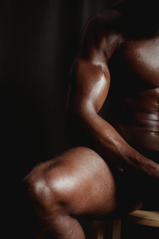 a man sitting on top of a wooden chair, an album cover, inspired by Hans Erni, pexels contest winner, hyperrealism, sexy muscular body, deep black skin, thighs close up, 30 year old man :: athletic