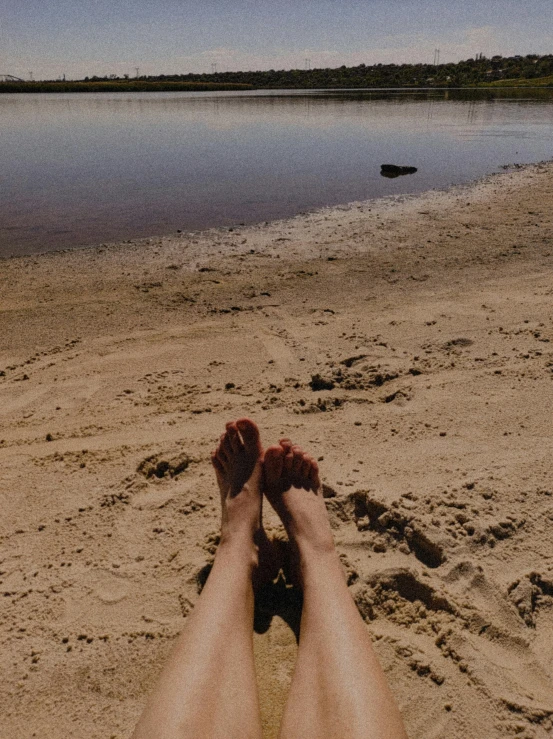 a person laying on a beach with their feet in the sand, red lake, profile image, sydney hanson, slightly pixelated