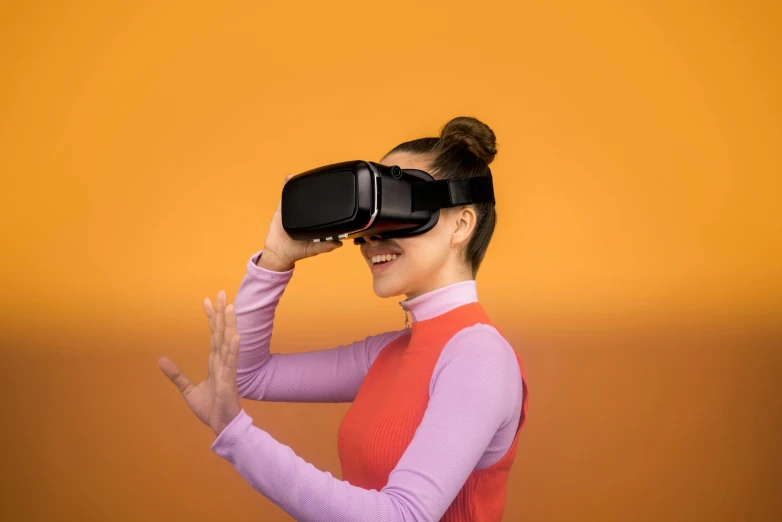 a woman in a pink shirt is using a virtual reality device, trending on pexels, interactive art, in front of an orange background, avatar image, glass visor, black