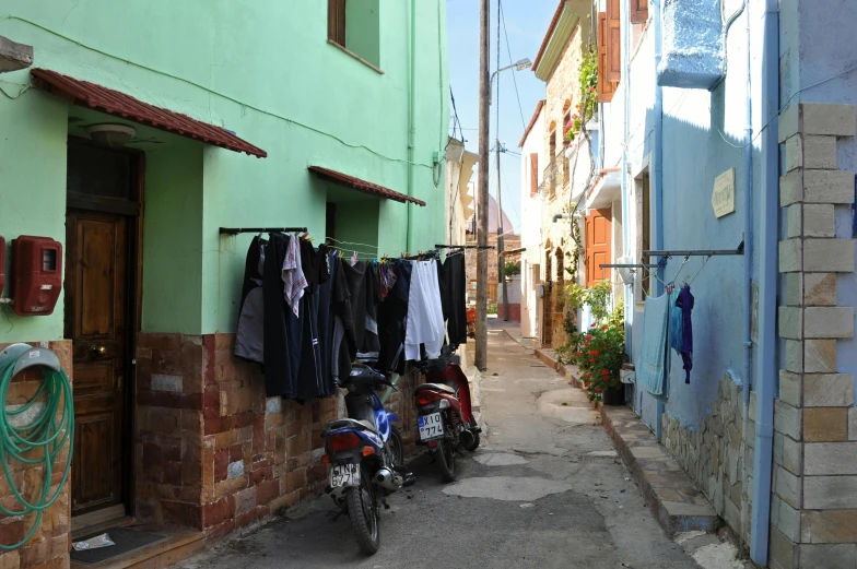 a motorcycle parked in front of a green building, by Meredith Dillman, pexels contest winner, laundry hanging, cyprus, alley, panoramic shot
