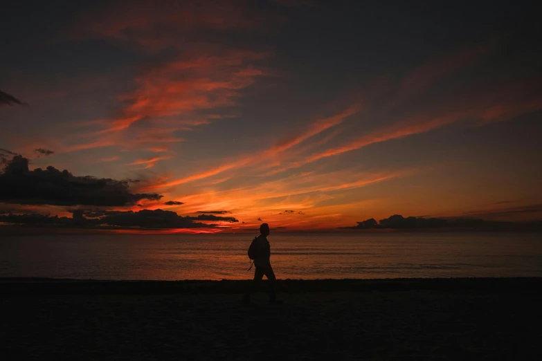 a man walking on the beach at sunset, pexels contest winner, red clouds, black silhouette, multicoloured, abel tasman