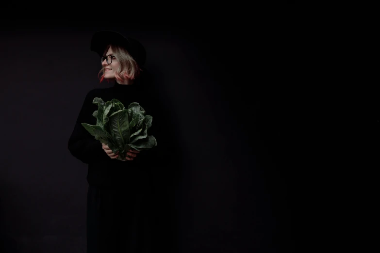 a woman in a black dress holding a bunch of broccoli, by Emma Andijewska, pexels contest winner, conceptual art, an old lady, lettuce, dressed in dark garment, man in black
