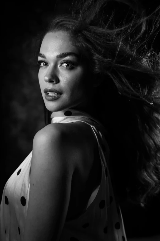 a woman with her hair blowing in the wind, a black and white photo, inspired by George Hurrell, hailee steinfeld, candid!! dark background, alexandria ocasio - cortez, medium format. soft light