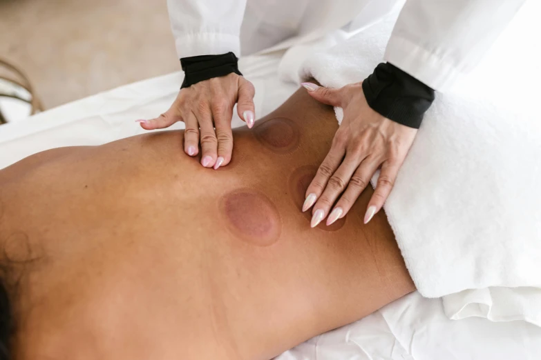 a woman getting a back massage at a spa, a photo, trending on pexels, process art, circles, moonlight showing injuries, scales covering her chest, 3/4 view from below