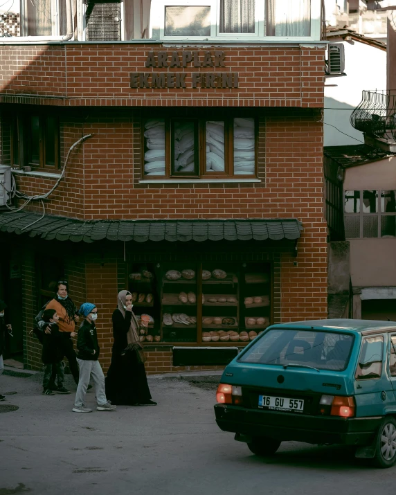 a car driving down a street next to a building, bosnian, bread, vintage aesthetic, group of people