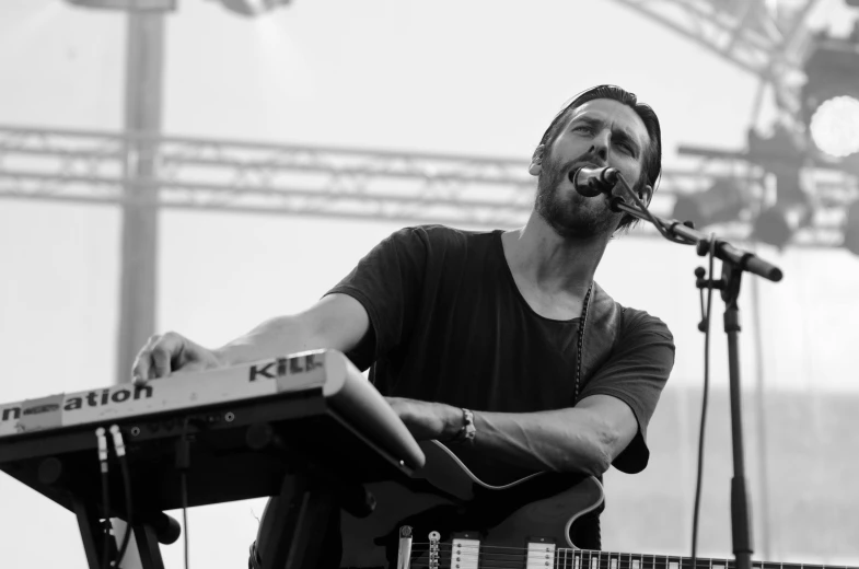 a man that is standing in front of a keyboard, a black and white photo, by Mathias Kollros, music festival, rounded beak, meadows, band