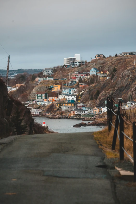 a road going down a hill next to a body of water, happening, waterfront houses, rugged, muted coloures, high-quality photo