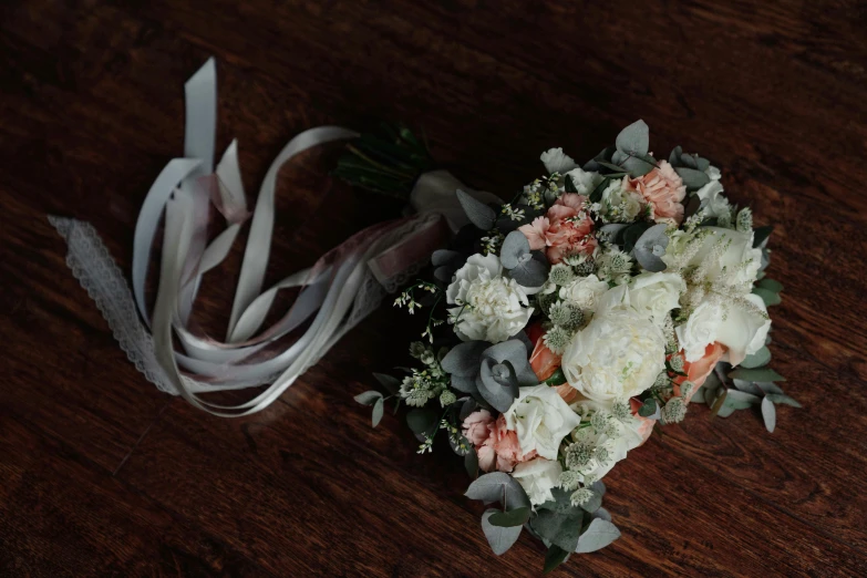 a bouquet of flowers sitting on top of a wooden table, white ribbon, muted colours, “ iron bark, medium level shot