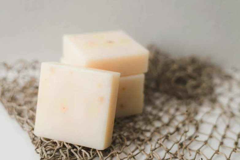 a couple of soap bars sitting on top of a net, a portrait, unsplash, white with chocolate brown spots, light orange mist, jen atkin, piled around