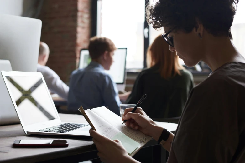 a person writing on a piece of paper in front of a laptop, trending on pexels, academic art, standing in class, avatar image, 9 9 designs, lachlan bailey