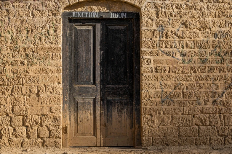 an old stone building with a black door, an album cover, by John Hutton, unsplash, australian tonalism, cyprus, sandstone, doors to various bedrooms, high details photo