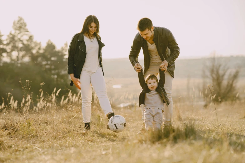 a family playing with a soccer ball in a field, pexels contest winner, leather clothing, avatar image, husband wife and son, white