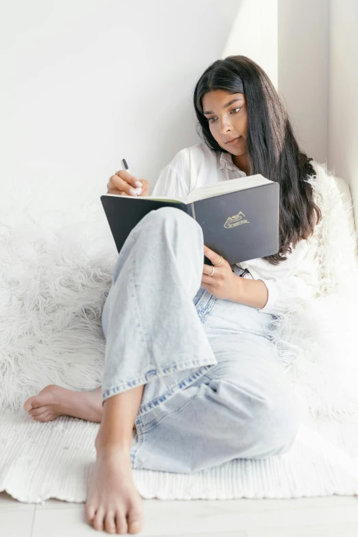 a woman sitting on a bed reading a book, inspired by Ruth Jên, trending on pexels, happening, baggy jeans, female with long black hair, writing in journal, promo photo