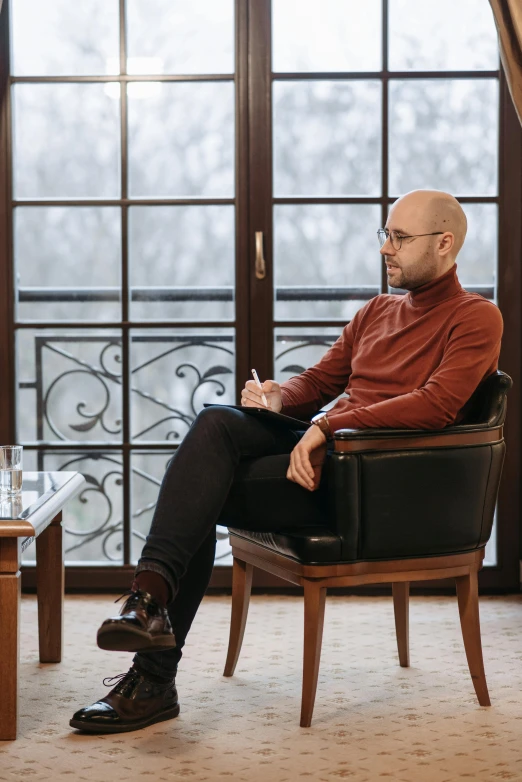 a man sitting in a chair in front of a window, sofya emelenko, a bald, jaquet droz, interview