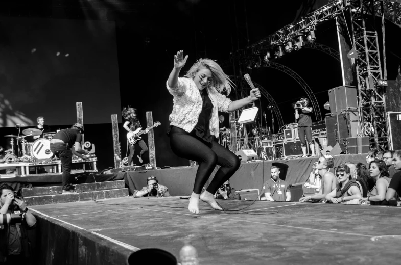 a woman dancing on a stage in front of a crowd, a black and white photo, by Tom Bonson, evanna lynch, rapping on stage at festival, rock, jump pose