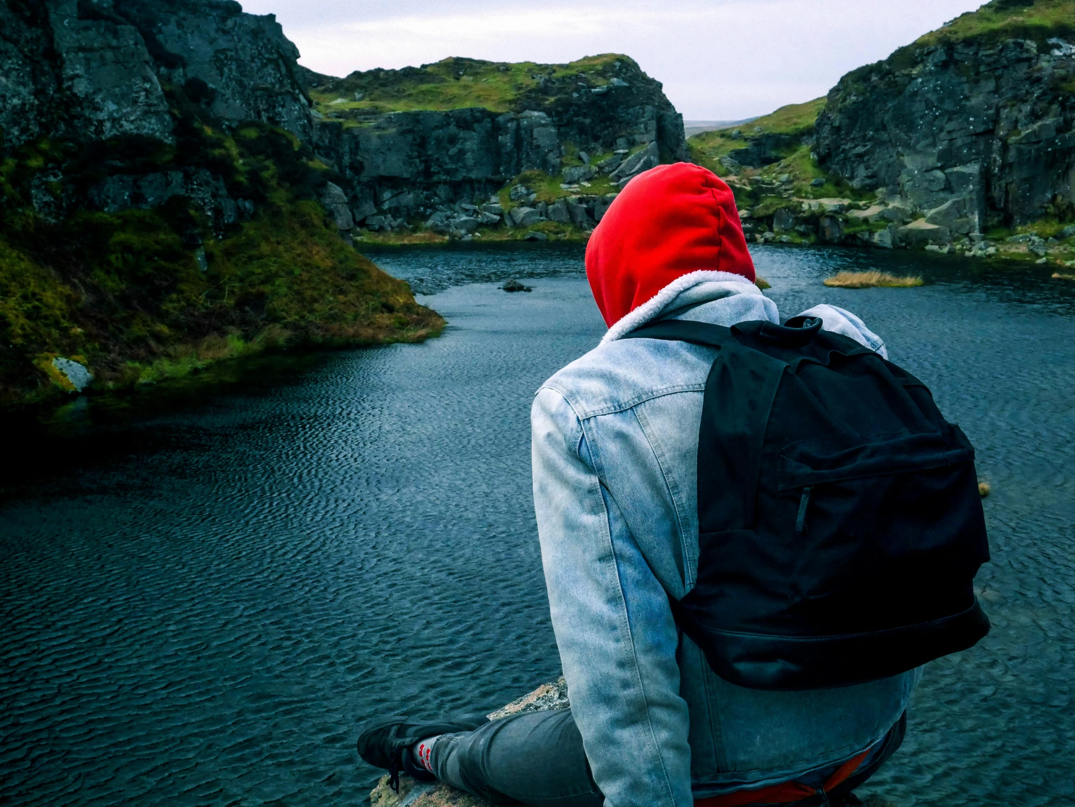 a person sitting on a rock overlooking a body of water, happening, red backwards cap, icelandic valley, sitting at a pond, traveling clothes