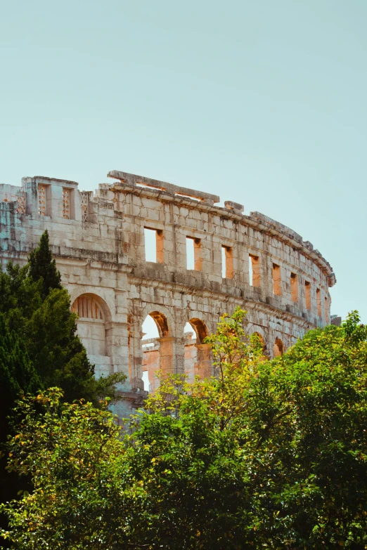 a large building sitting on top of a lush green hillside, pexels contest winner, neoclassicism, colosseum, built into trees and stone, sunfaded, promo image