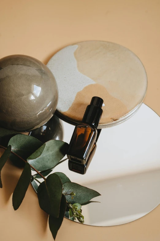 a bottle of essential oil sitting on top of a white plate, a still life, inspired by Ceferí Olivé, trending on unsplash, bauhaus, round mirror on the wall, earth tone color scheme, obsidian globe, skincare